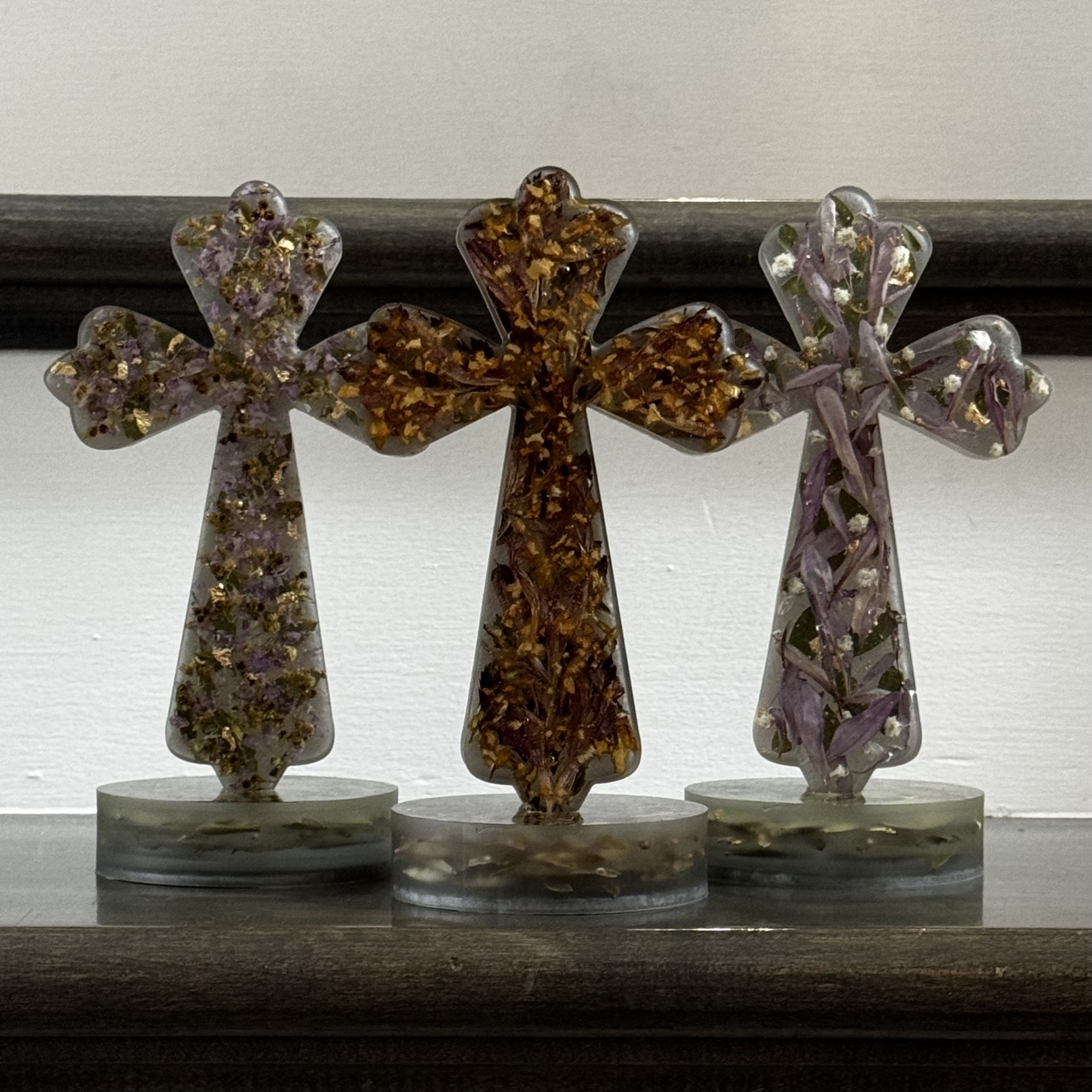 Three resin crosses filled with preserved flowers and gold flakes
